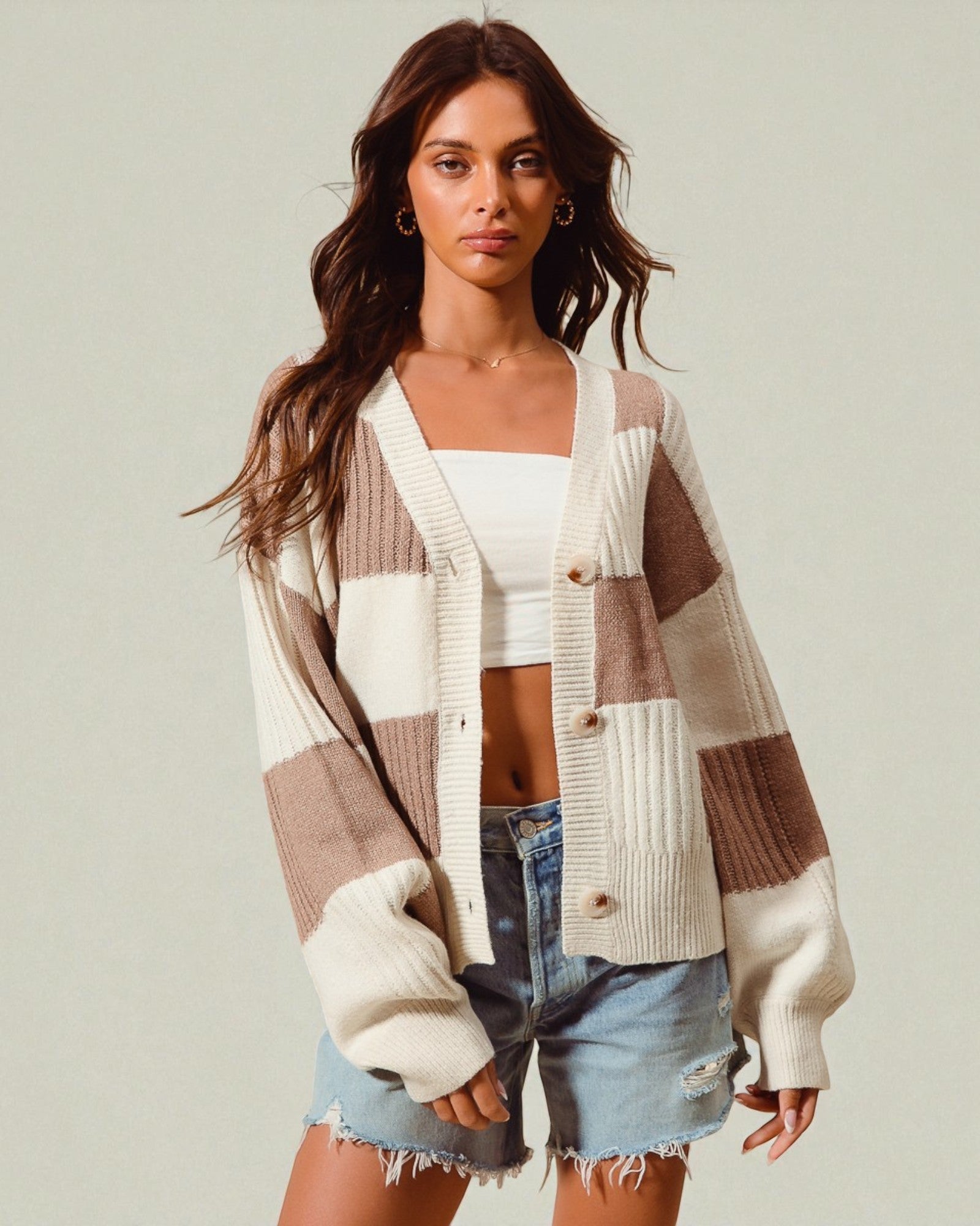 Woman wearing a plaid cardigan over a white top and denim shorts on a plain background