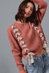 Woman wearing a pink sweater with decorative bows, standing against a gray background