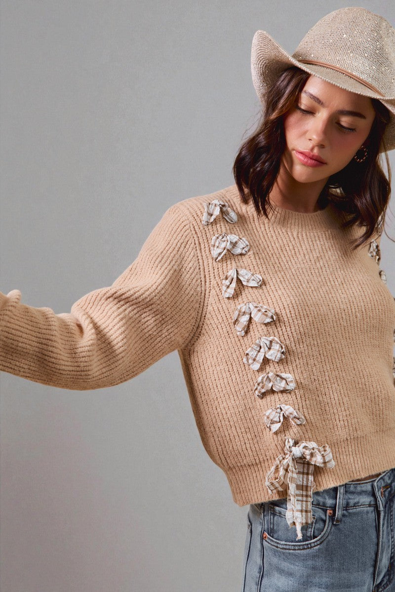 Woman wearing a beige sweater with decorative bows and a matching hat against a gray background