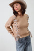 Woman wearing a beige sweater with floral embellishments, blue jeans, and a hat on a white background