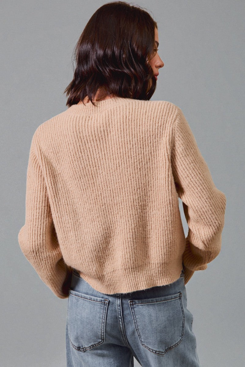 Person wearing a beige sweater and blue jeans against a gray background