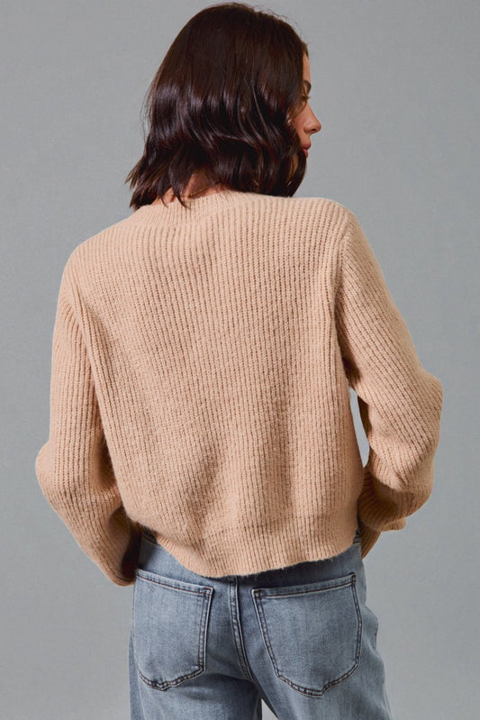 Person wearing a beige sweater and blue jeans against a gray background