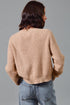 Person wearing a beige sweater and blue jeans against a gray background