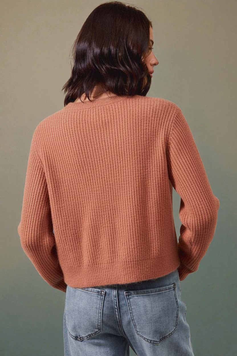 Person wearing a brown ribbed sweater and blue jeans against a green background