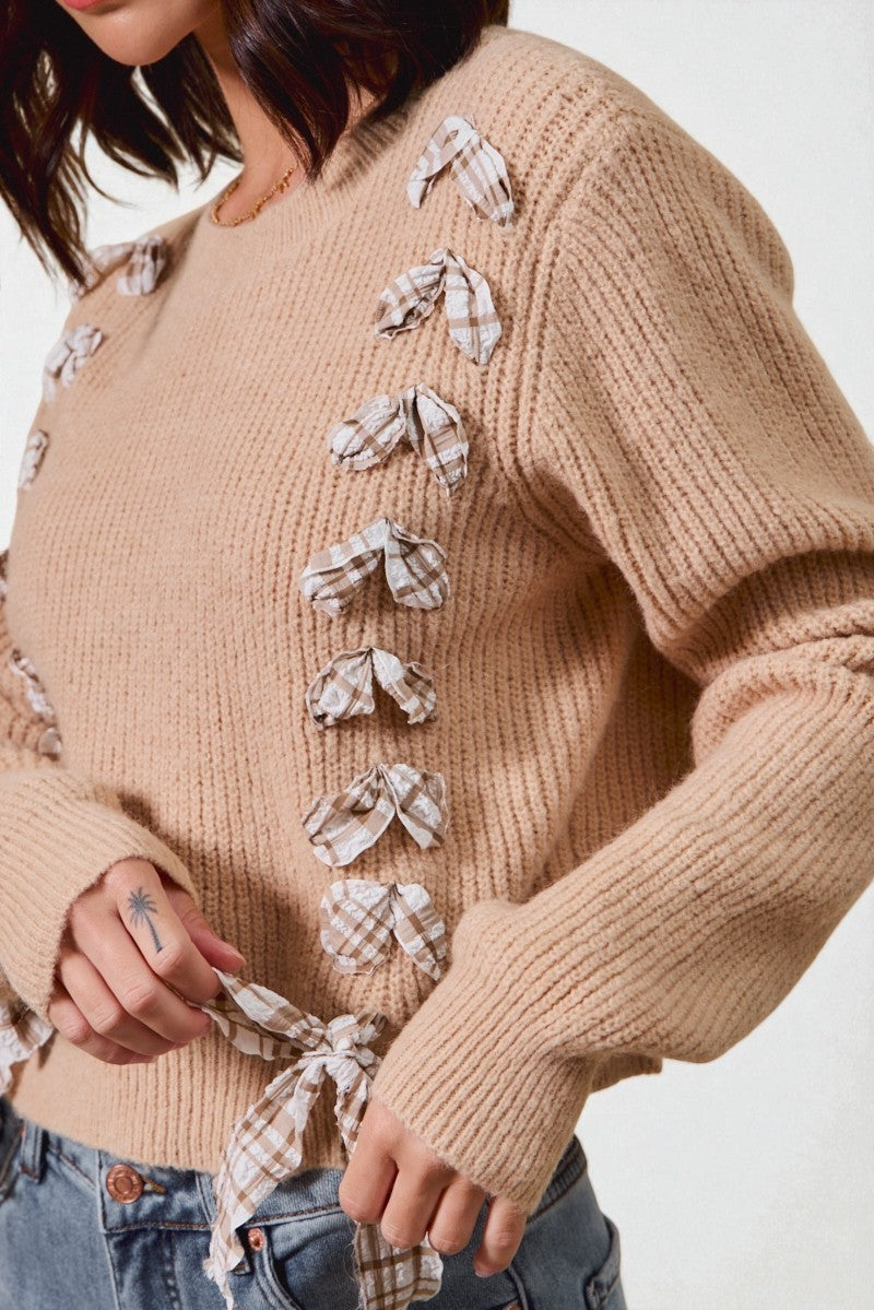 Beige sweater with plaid bow details worn by a person on a white background