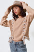 Woman wearing a beige sweater with bow details and a wide-brimmed hat on a white background