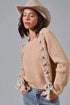 Woman wearing a beige sweater with bow details, denim jeans, and a beige hat on a gray background