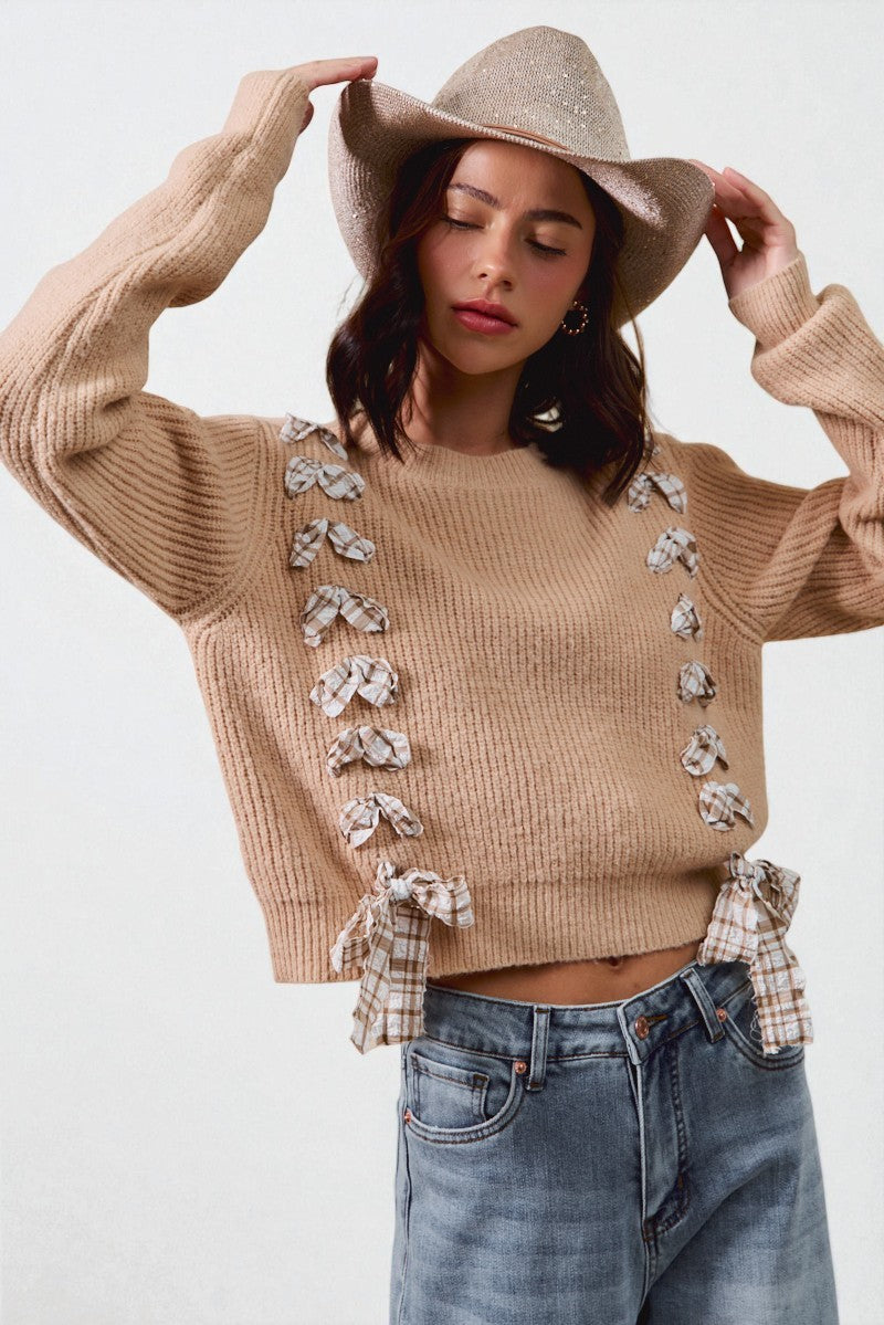 Woman wearing a beige sweater with floral embellishments, blue jeans, and a beige hat on a white background
