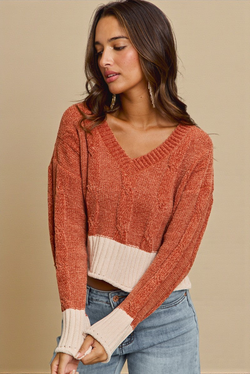 Woman wearing a rust-colored sweater with a white trim on a beige background