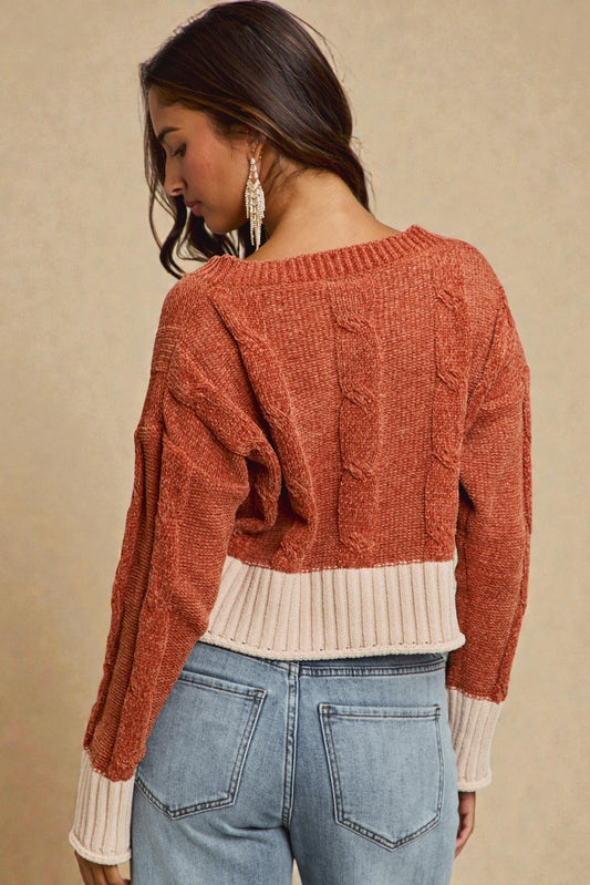 Woman wearing a rust-colored sweater over a cream shirt with blue jeans on a beige background