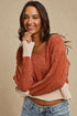 Woman wearing a rust-colored sweater over a beige top with blue jeans on a beige background