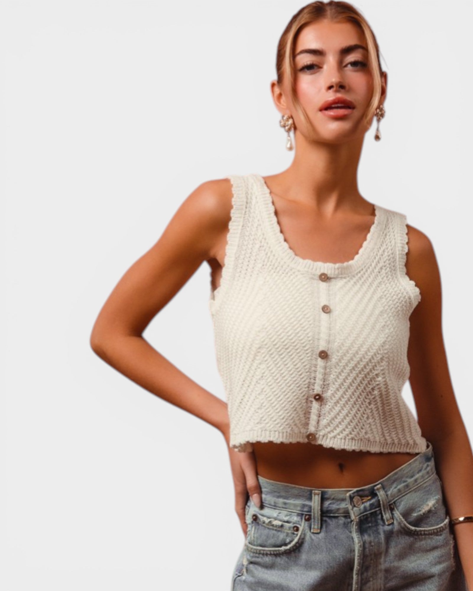 Woman wearing a cream knitted crop top and jeans on a plain background
