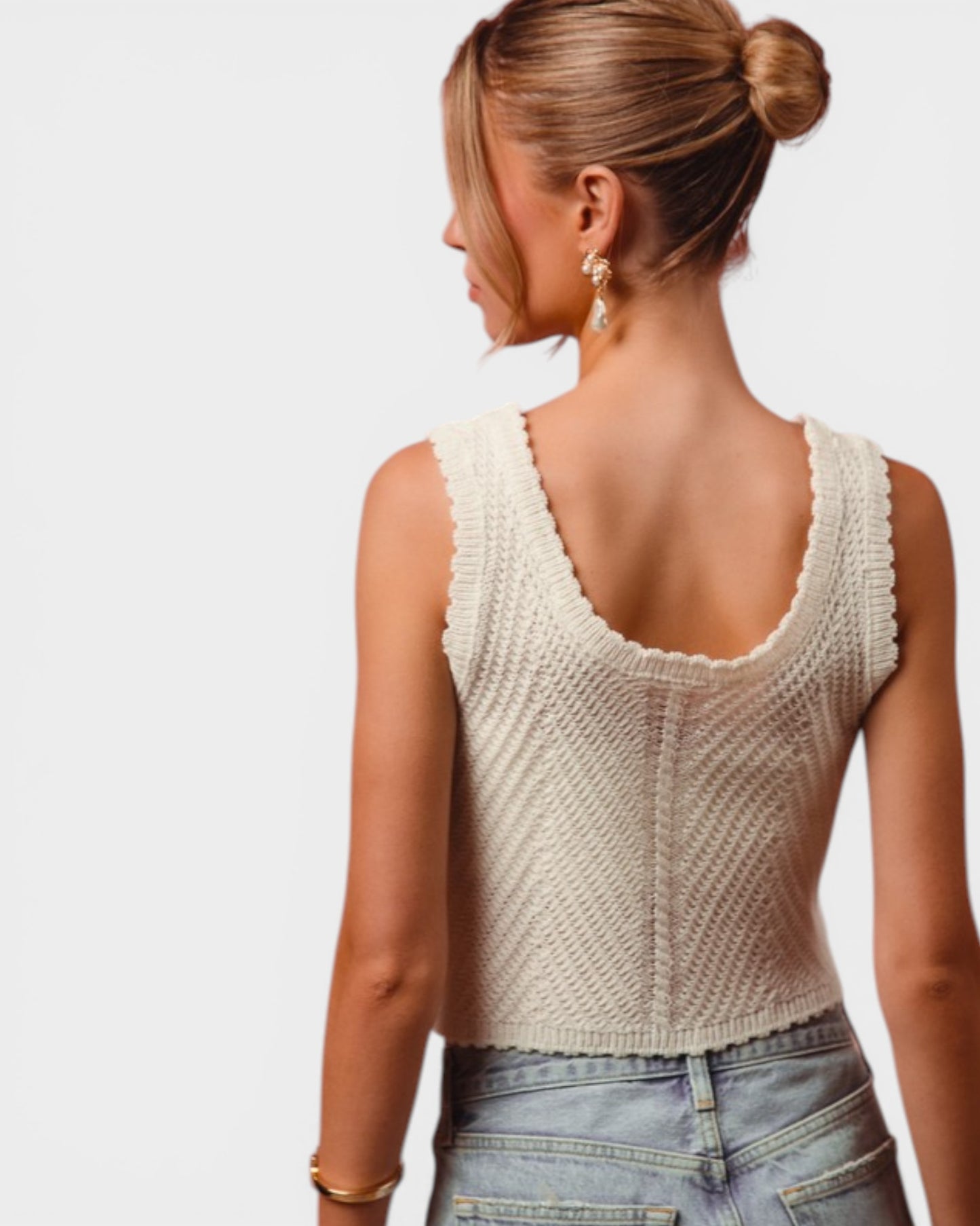 Woman wearing a beige knitted tank top and blue jeans on a plain background