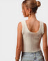 Woman wearing a beige knitted tank top and blue jeans on a plain background