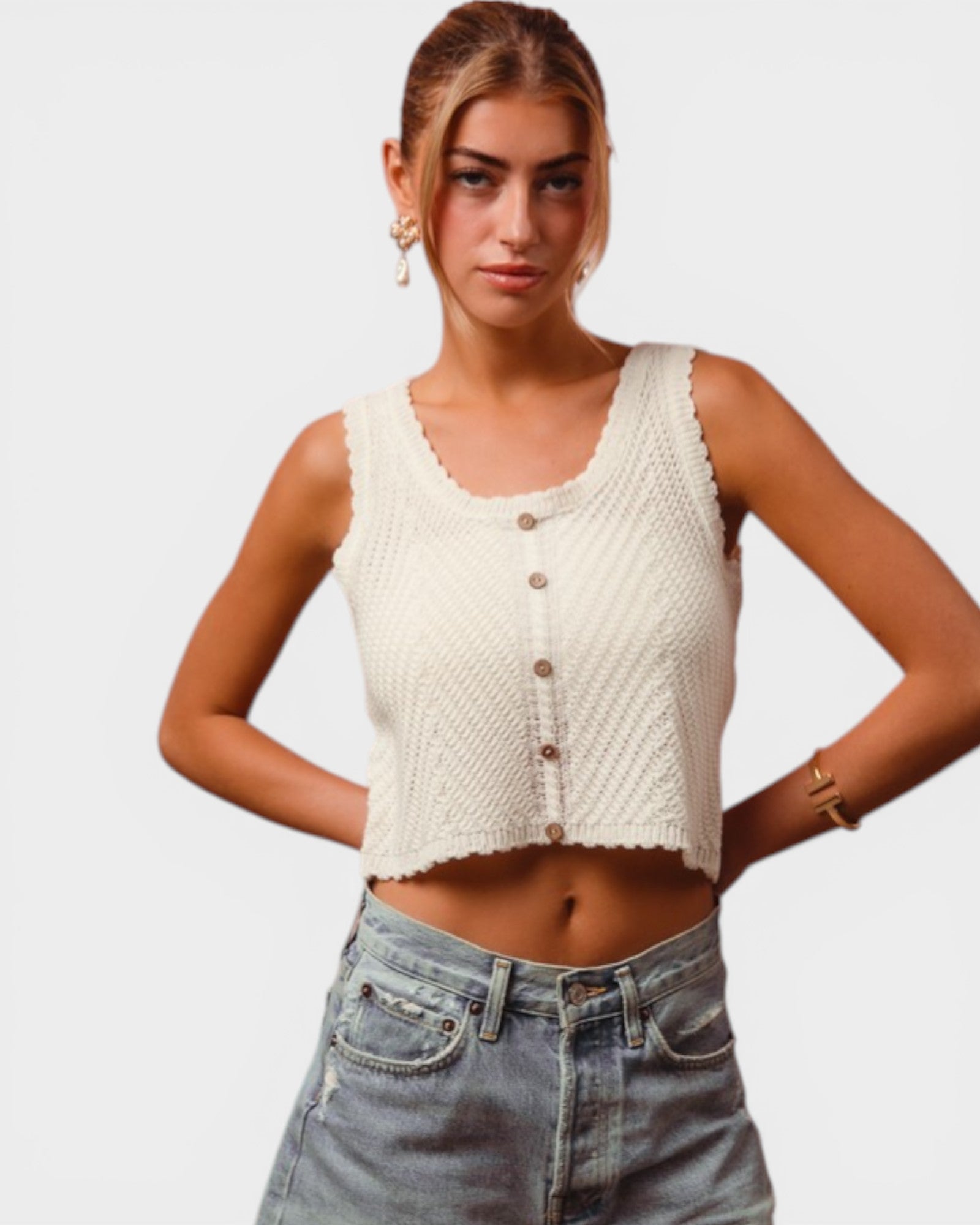 Woman wearing a white knitted tank top and blue jeans on a plain background