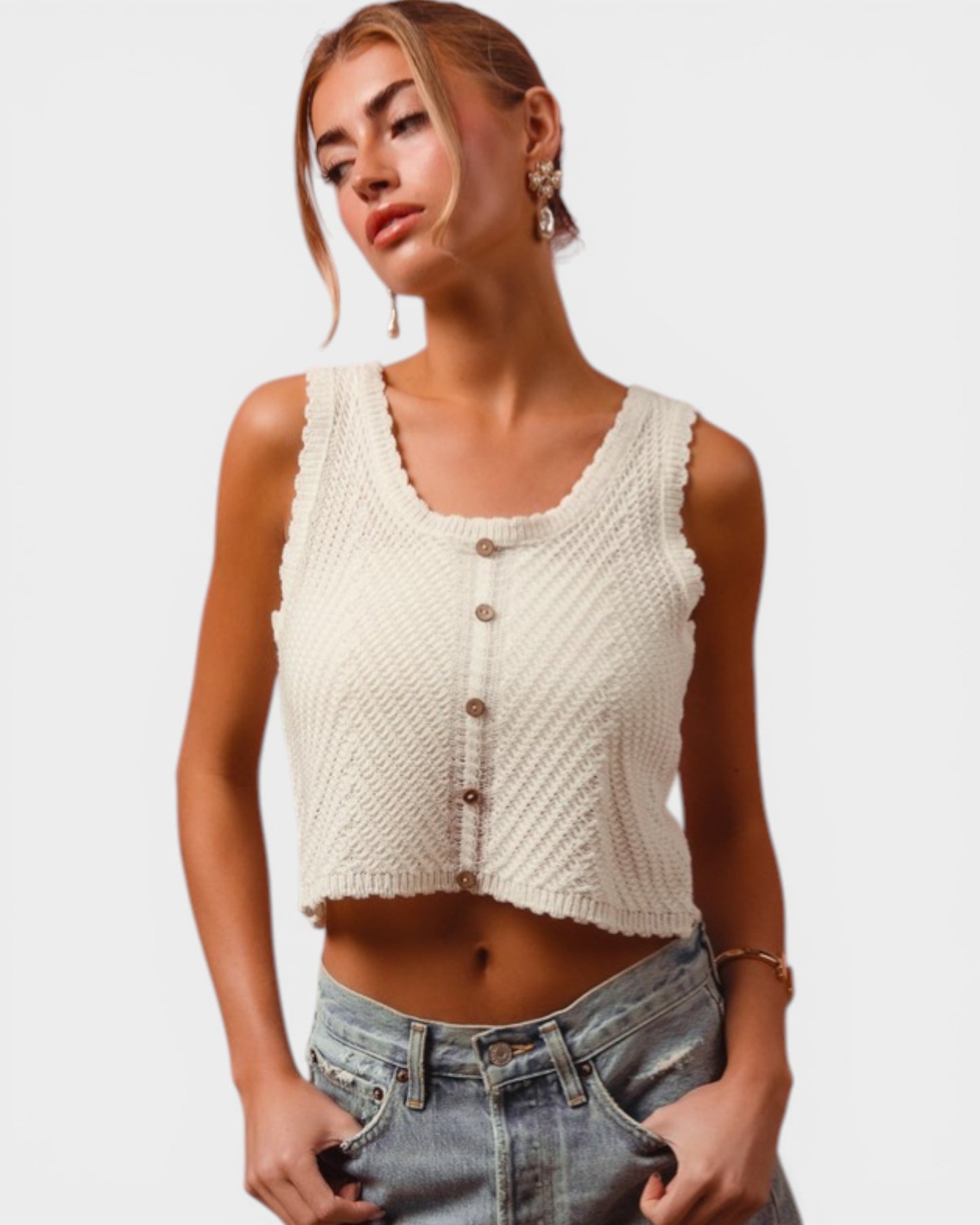 Woman wearing a cream knitted tank top and blue jeans on a plain background