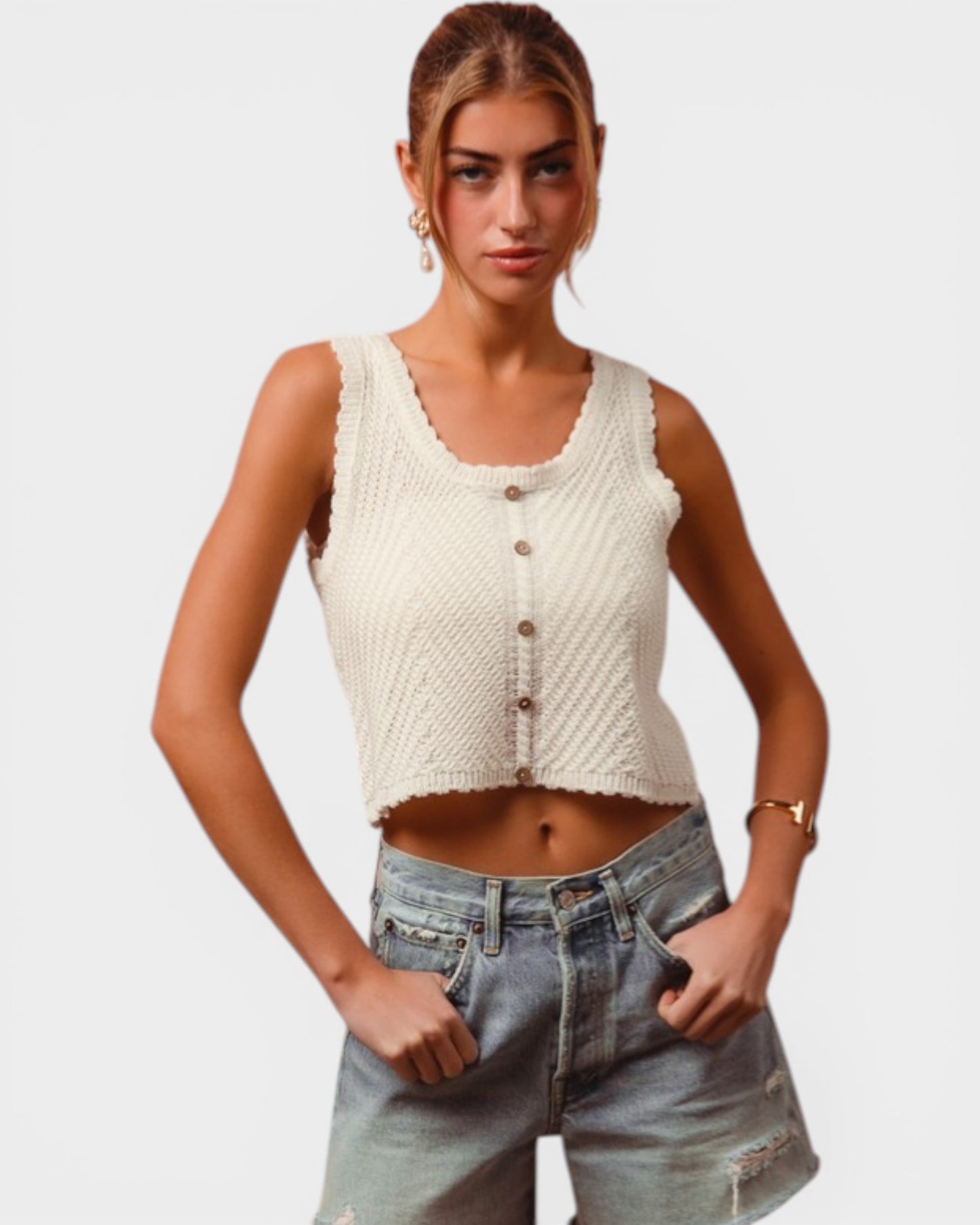 Woman wearing a cream knitted vest and denim shorts on a plain background