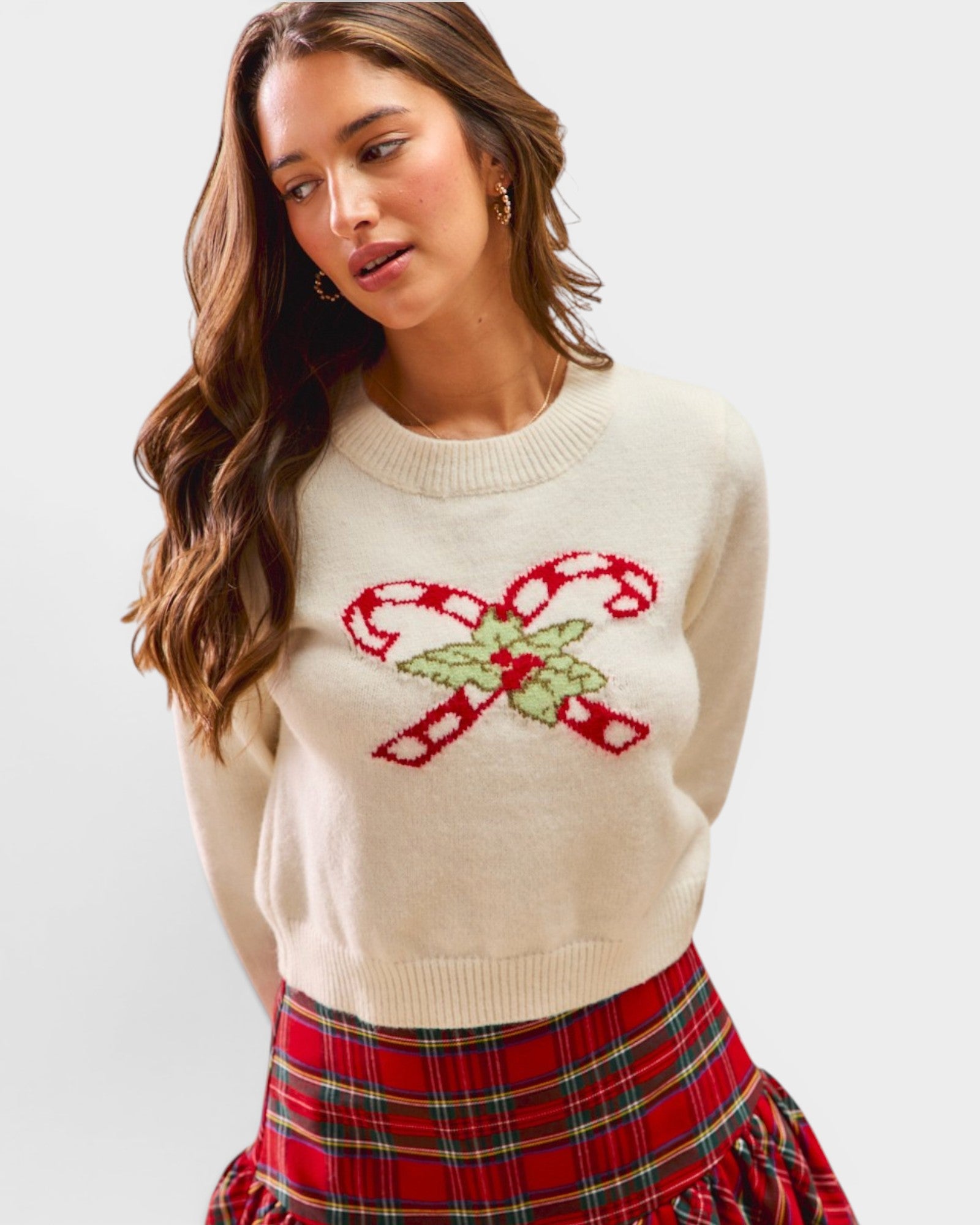 Woman wearing a cream sweater with candy cane design and plaid skirt on a white background