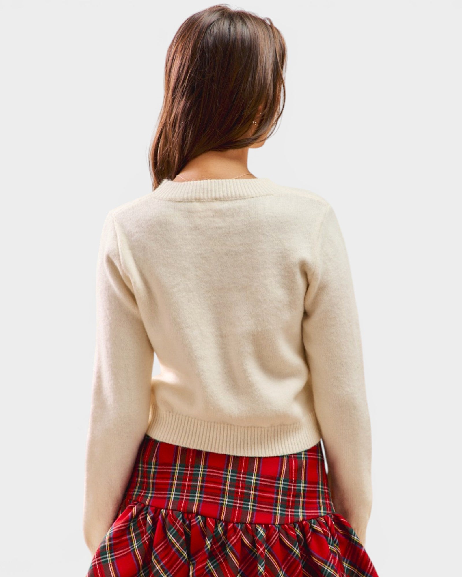 Person wearing a beige sweater and red plaid skirt on a white background