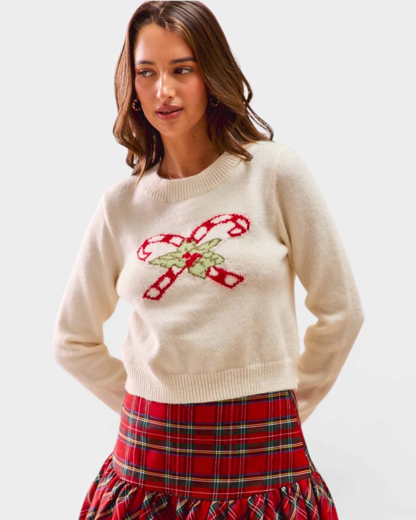 Woman wearing a cream sweater with candy cane design and a red plaid skirt on a white background