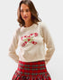 Woman wearing a cream sweater with candy cane design and a red plaid skirt on a white background
