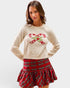 Woman wearing a cream sweater with candy cane design and a red plaid skirt on a white background