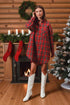 Woman in a red plaid dress and white boots standing in a festive room with Christmas decorations.