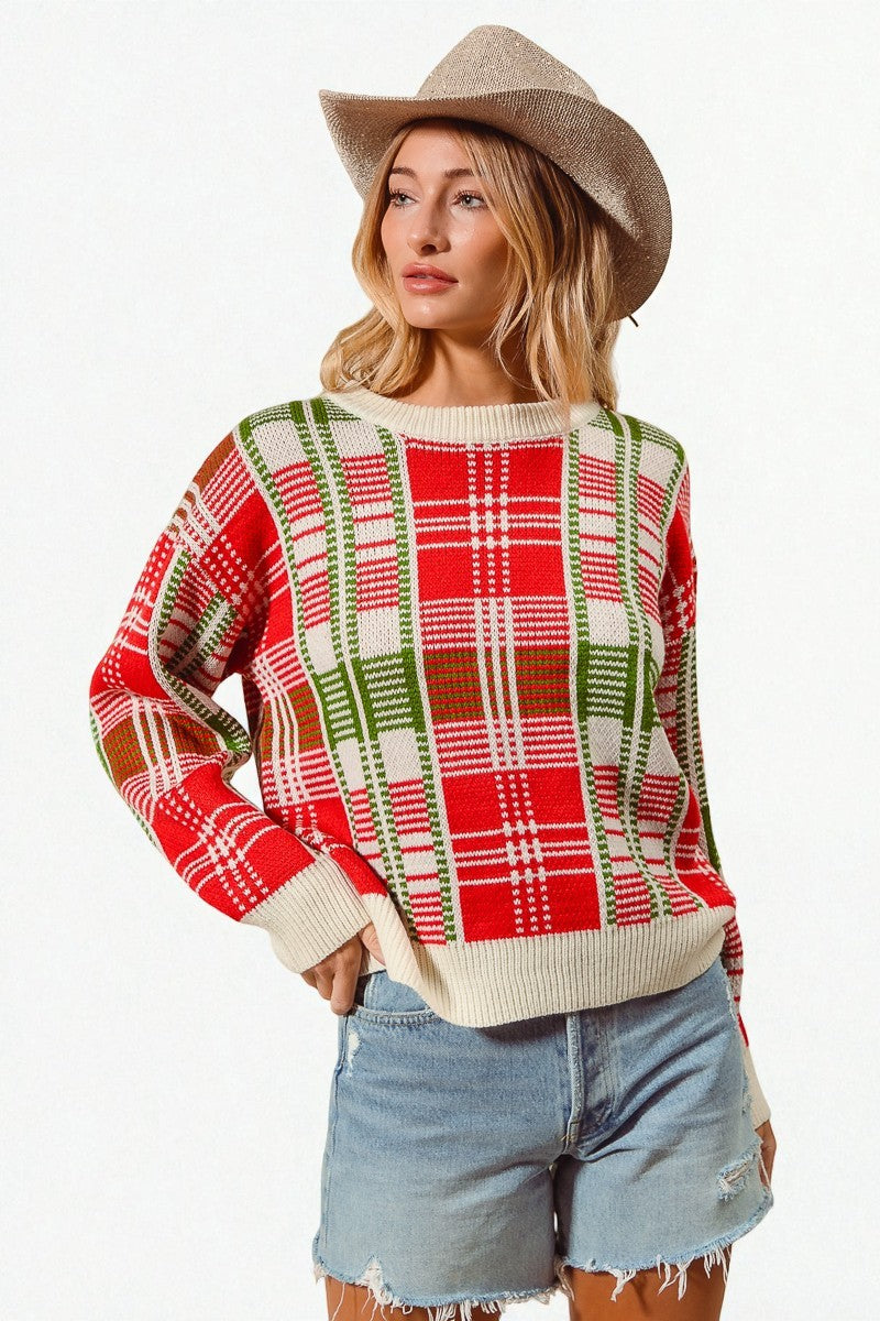 Woman wearing a red and green plaid sweater with denim shorts and a beige hat on a white background
