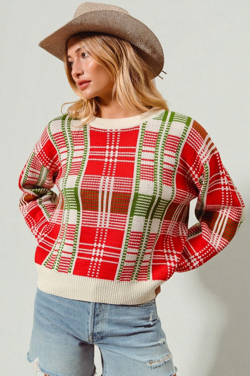 Person wearing a red and green plaid sweater with a beige hat and denim shorts on a light gray background