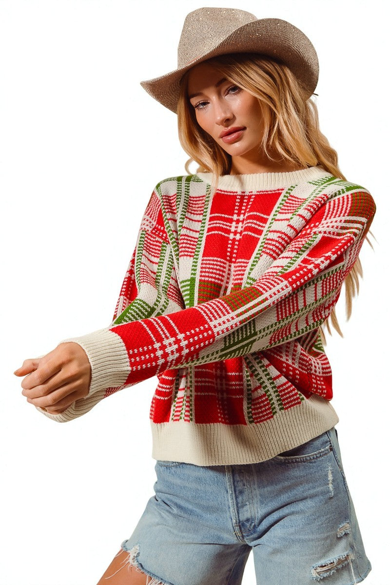 Woman wearing a plaid sweater with red, green, and beige patterns, paired with denim shorts and a hat.