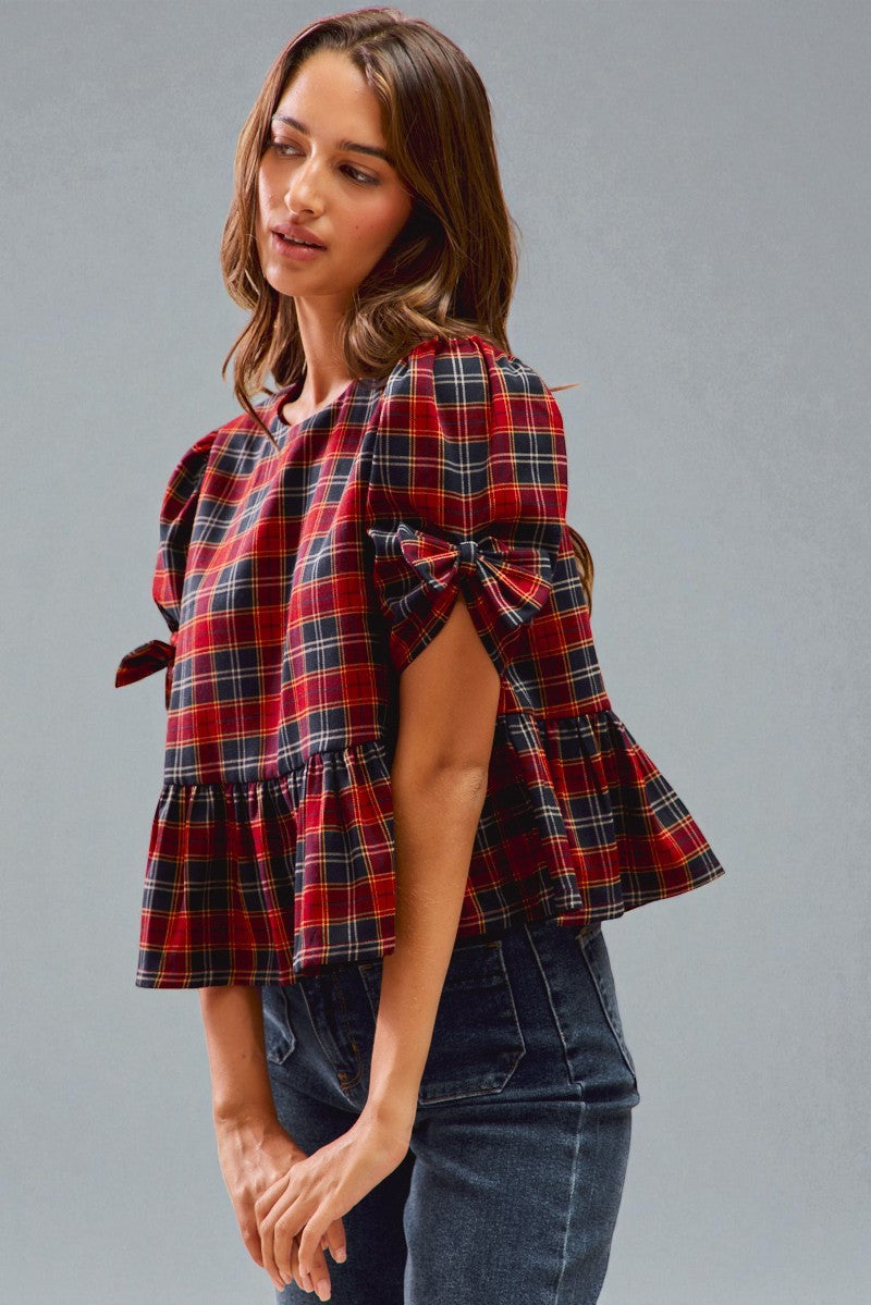 Woman wearing a red and blue plaid top with bell sleeves against a gray background