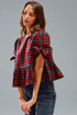 Woman wearing a red and blue plaid top with bell sleeves against a gray background