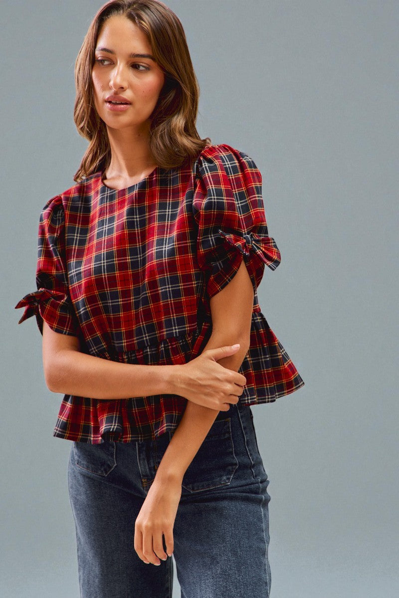 Woman wearing a red and black plaid top with ruffled sleeves against a gray background