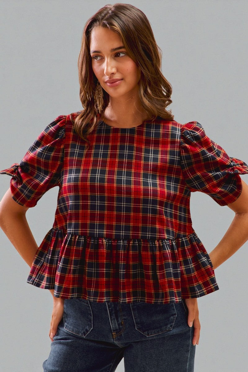 Woman wearing a red plaid top with ruffled sleeves and hem against a gray background