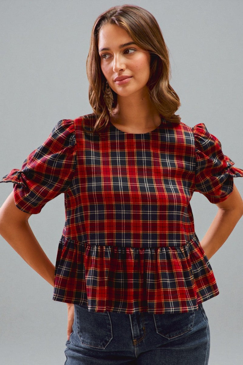 Woman wearing a red plaid blouse with puffed sleeves against a gray background