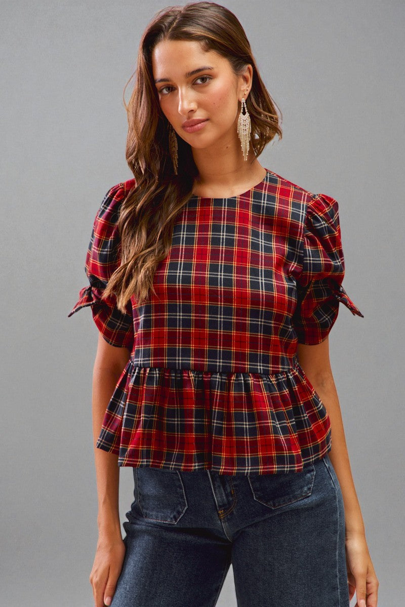 Woman wearing a red and blue plaid top with puffed sleeves against a gray background
