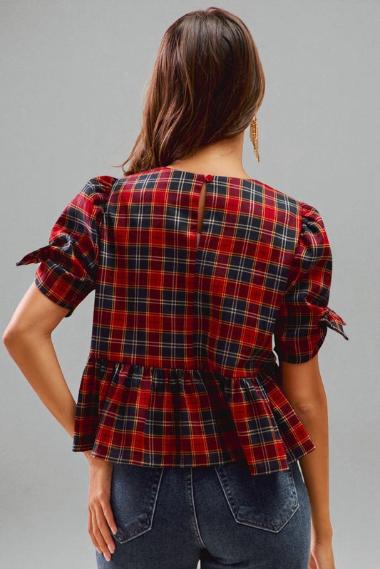 Woman wearing a red and black plaid top with ruffled sleeves on a gray background