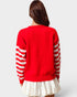 Person wearing a red sweater with white stripes on sleeves and a white skirt against a light gray background