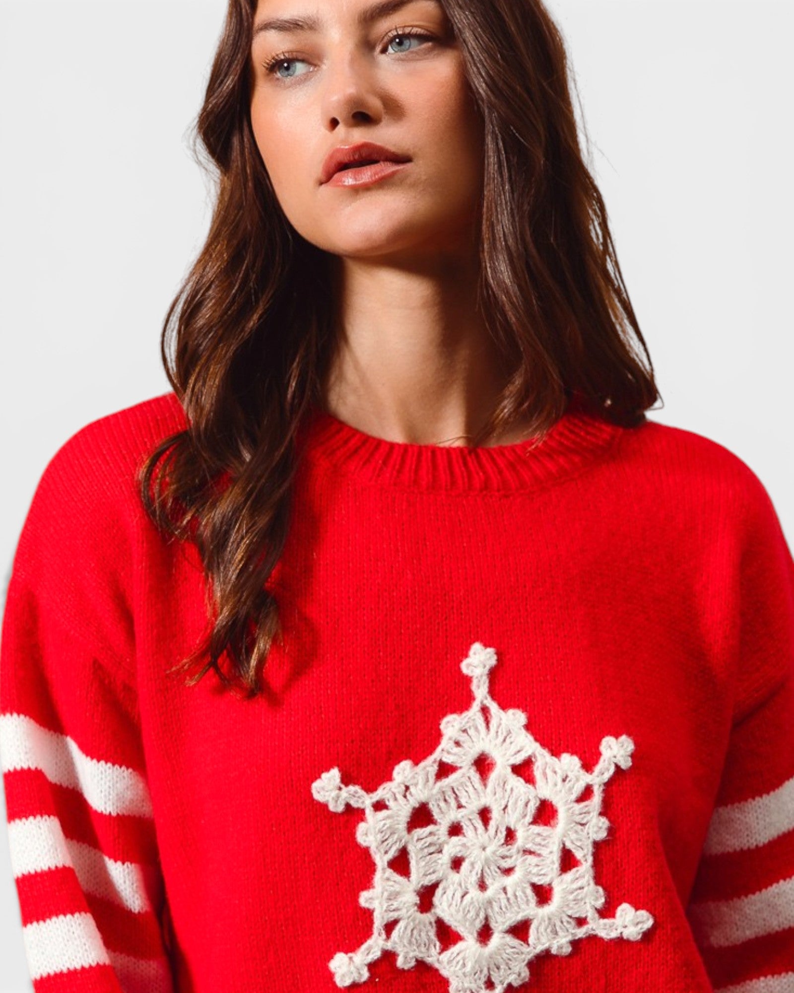 Woman wearing a red sweater with a white snowflake design on a plain background