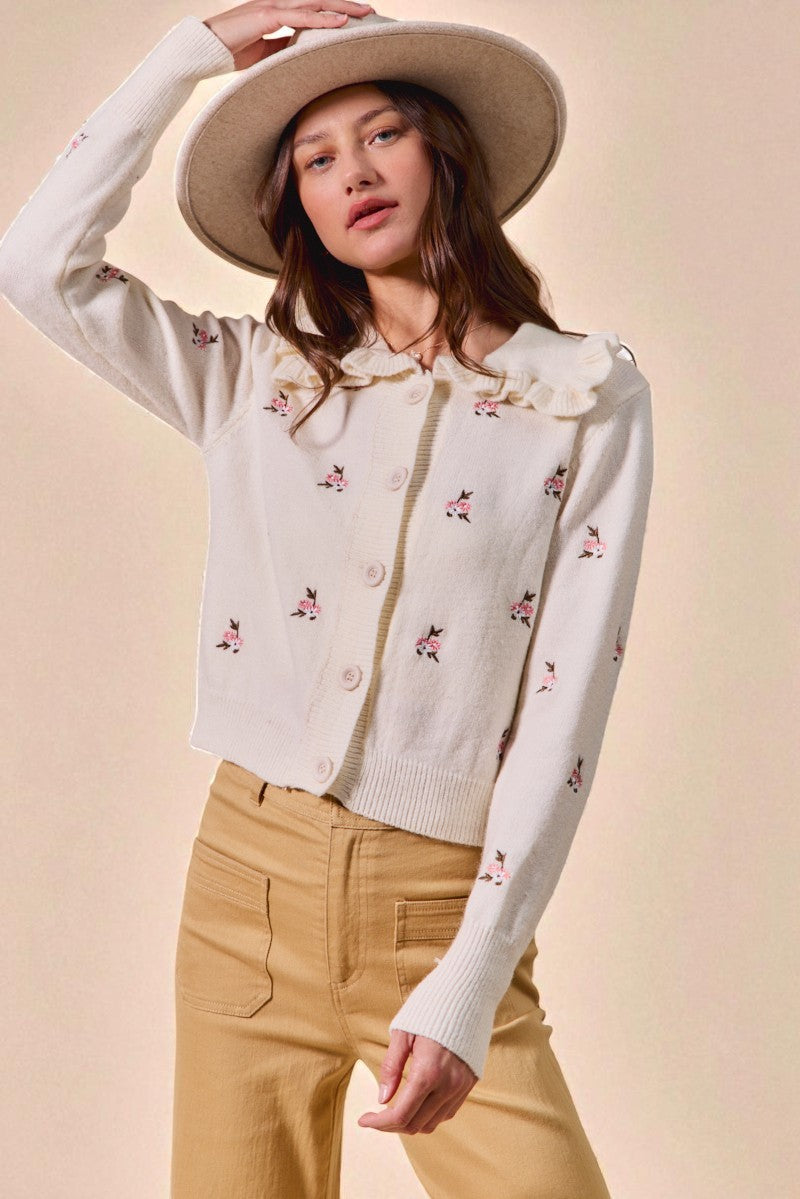 Woman wearing a white embroidered cardigan and beige pants with a beige hat on a beige background