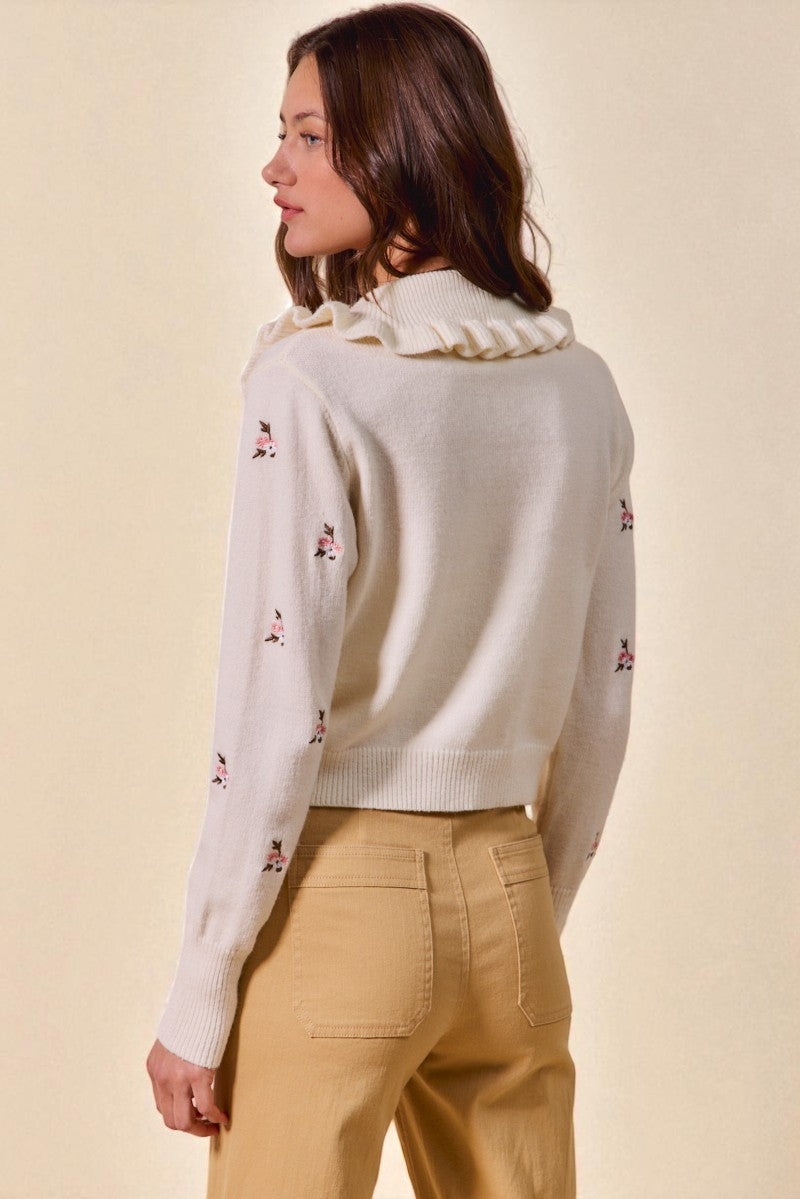 Woman wearing a cream-colored sweater with floral embroidery on a beige background