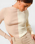 Woman wearing a beige ribbed sweater and pants against a light background