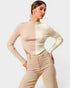 Woman wearing a two-tone beige sweater and pants against a plain background
