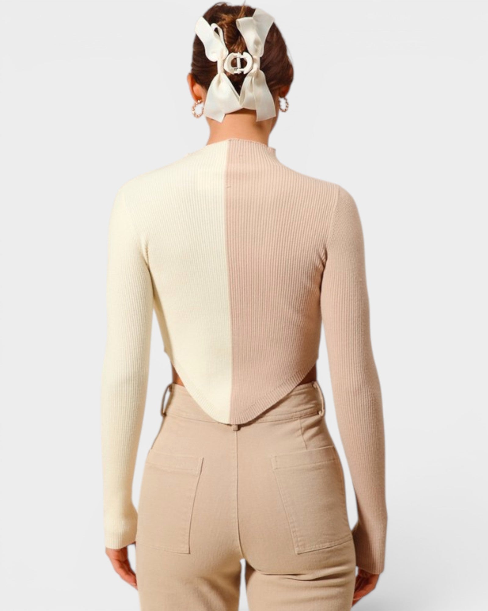 Person wearing a beige and cream ribbed sweater with a cutout design on a white background