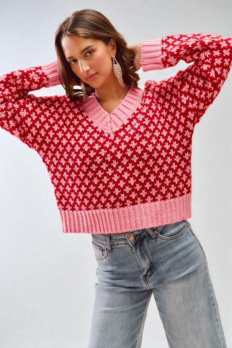 Person wearing a red and pink patterned sweater with blue jeans on a white background