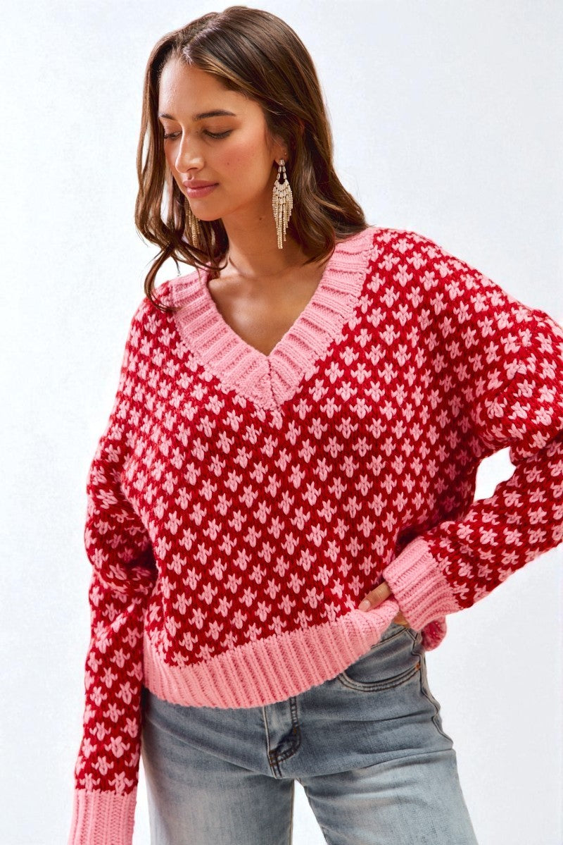 Woman wearing a red and pink patterned sweater with blue jeans on a white background
