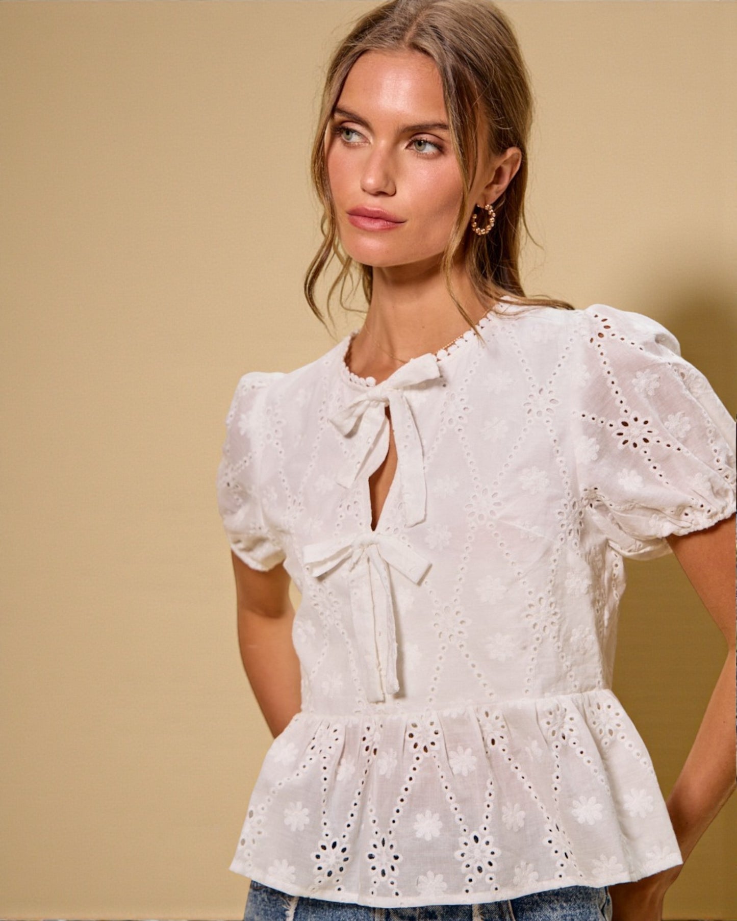 Woman wearing a white lace blouse with puff sleeves against a beige background