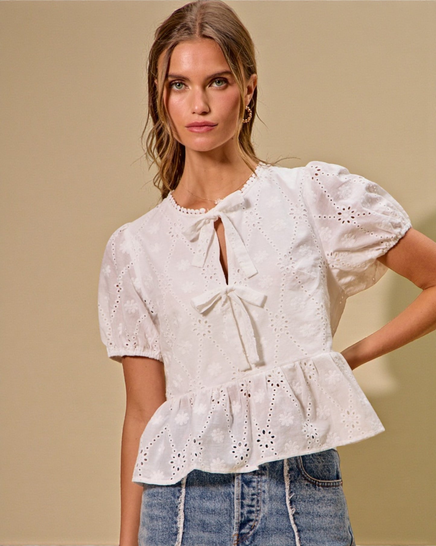 Woman wearing a white blouse with ruffled details against a beige background