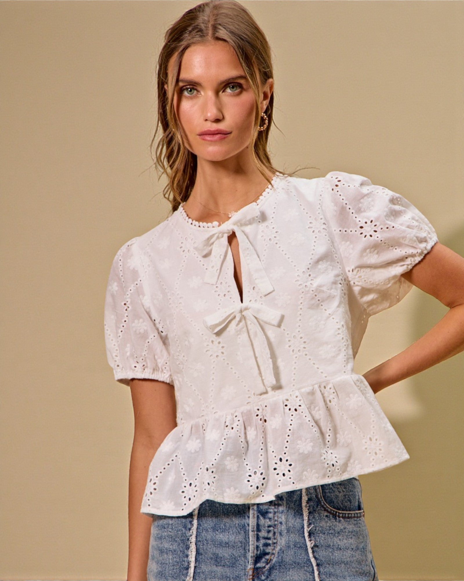 Woman wearing a white blouse with ruffled details against a beige background