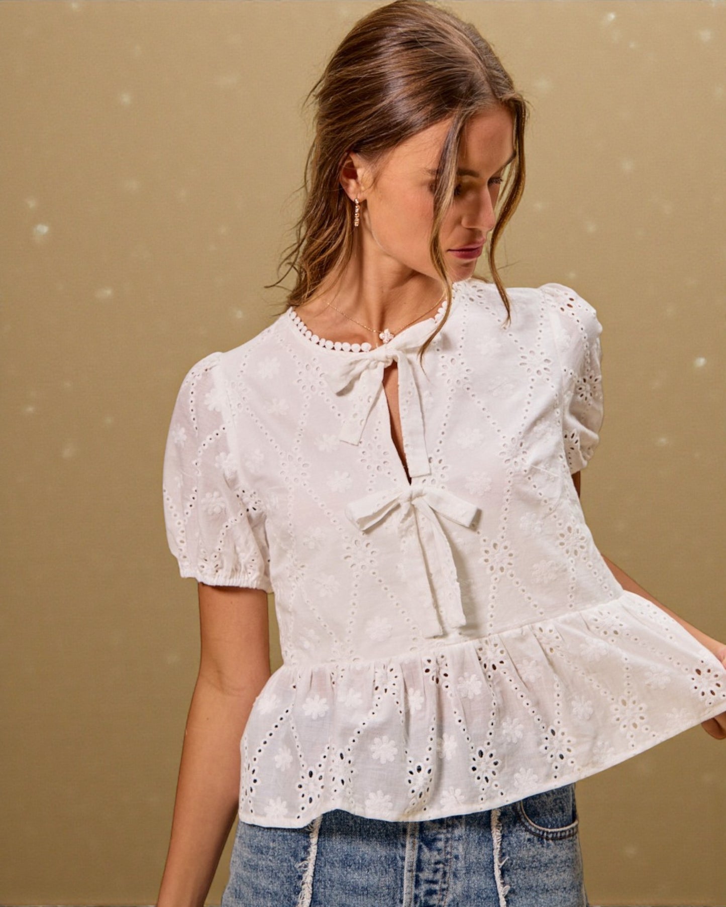 Woman wearing a white blouse with a tie detail against a beige background